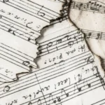 Imagem de pedaços antigos de partitura musical ilustrando a história da música