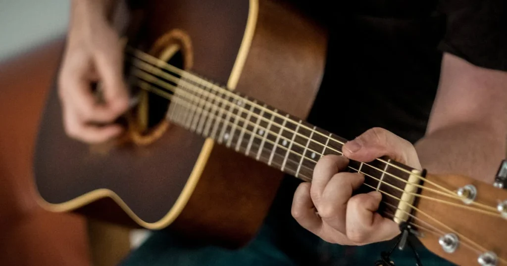 Imagem de um homem tocando violão, fazendo um acorde de dó maior