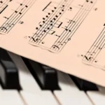 Imagem de uma folha de partitura em cima das teclas de um piano ou teclado musical ilustrando artigo de teoria musical