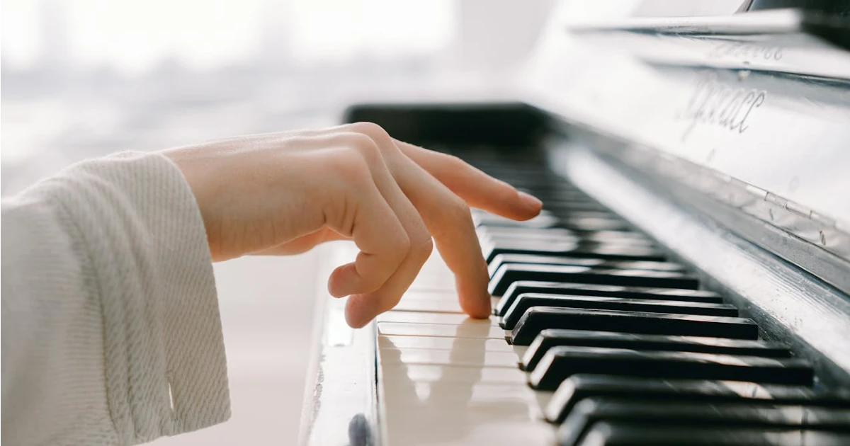 Imagem do dedo médio da mão direita de uma mulher encostando na tecla de um piano. Imagem usada para ilustrar tonalidade musical
