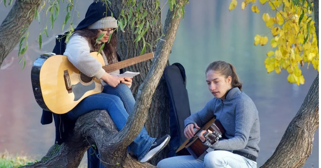 imagem de duas mulheres com violões em baixo de uma árvore para ilustrar a importância cultural e social dos gêneros de musica