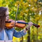mulher tocando violino em um lugar cheio de árvores. Imagem usada para ilustrar o artigo o que é melodia