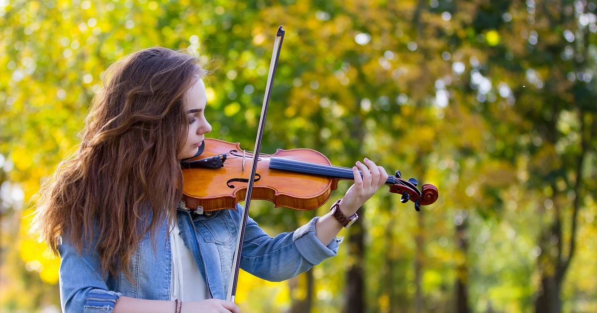 mulher tocando violino em um lugar cheio de árvores. Imagem usada para ilustrar o artigo o que é melodia