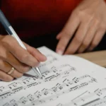 Imagem de uma pessoa rabiscando uma notação musical do tipo partitura com uma caneta.